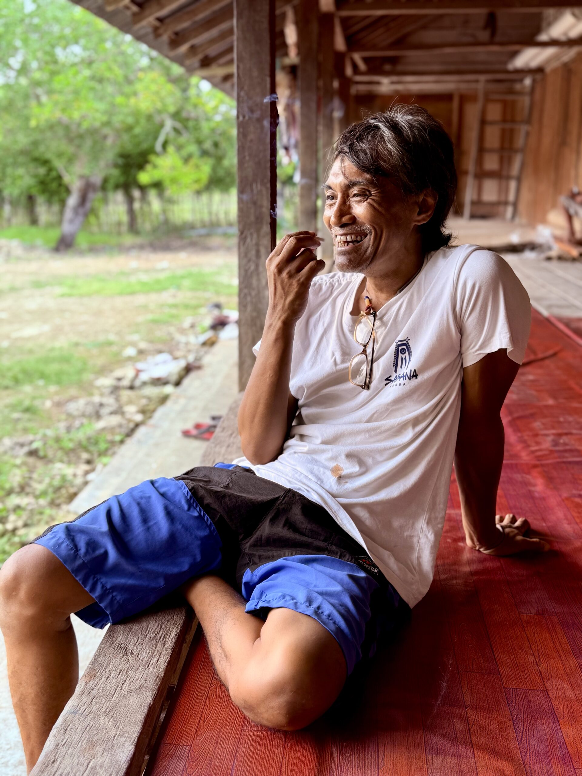 Portrait du guide local Umbu à Sumba, assis dans une maison traditionnelle de Sumba, incarnat l'accueil chaleureux et l'authenticité des habitants de l'île.