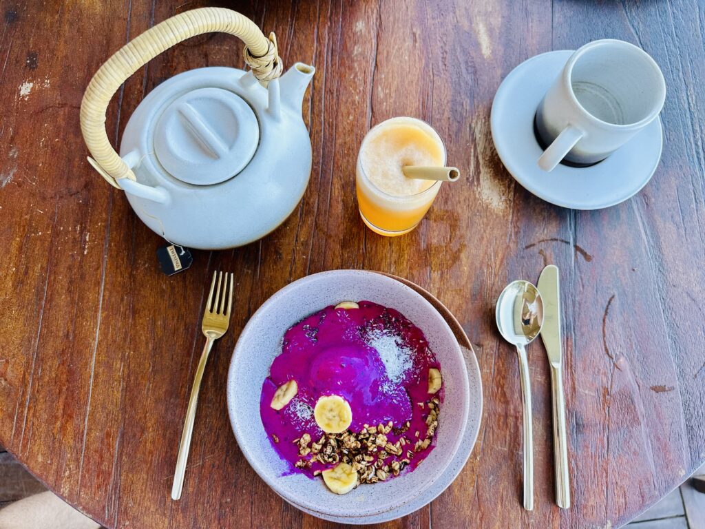 Petit-déjeuner coloré et sain, avec smoothie bowl, théière et jus de fruits frais sur une table en bois.