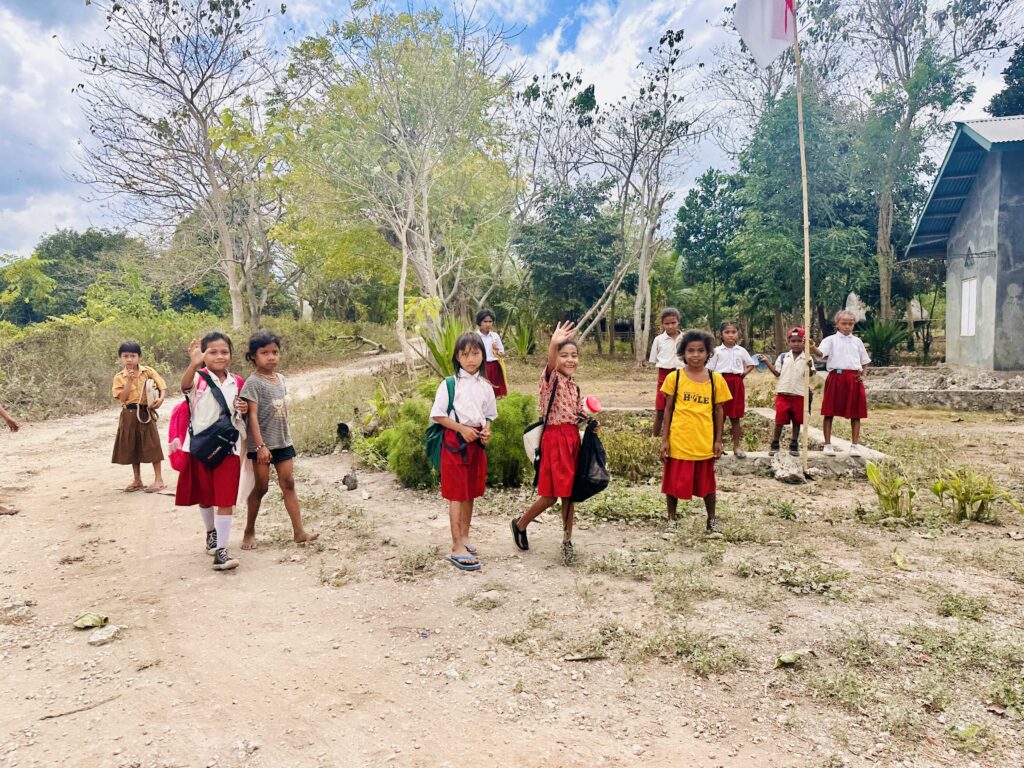 Groupe d'enfants de Sumba en uniforme scolaire souriants et saluant la caméra à l'extérieur d'une école.