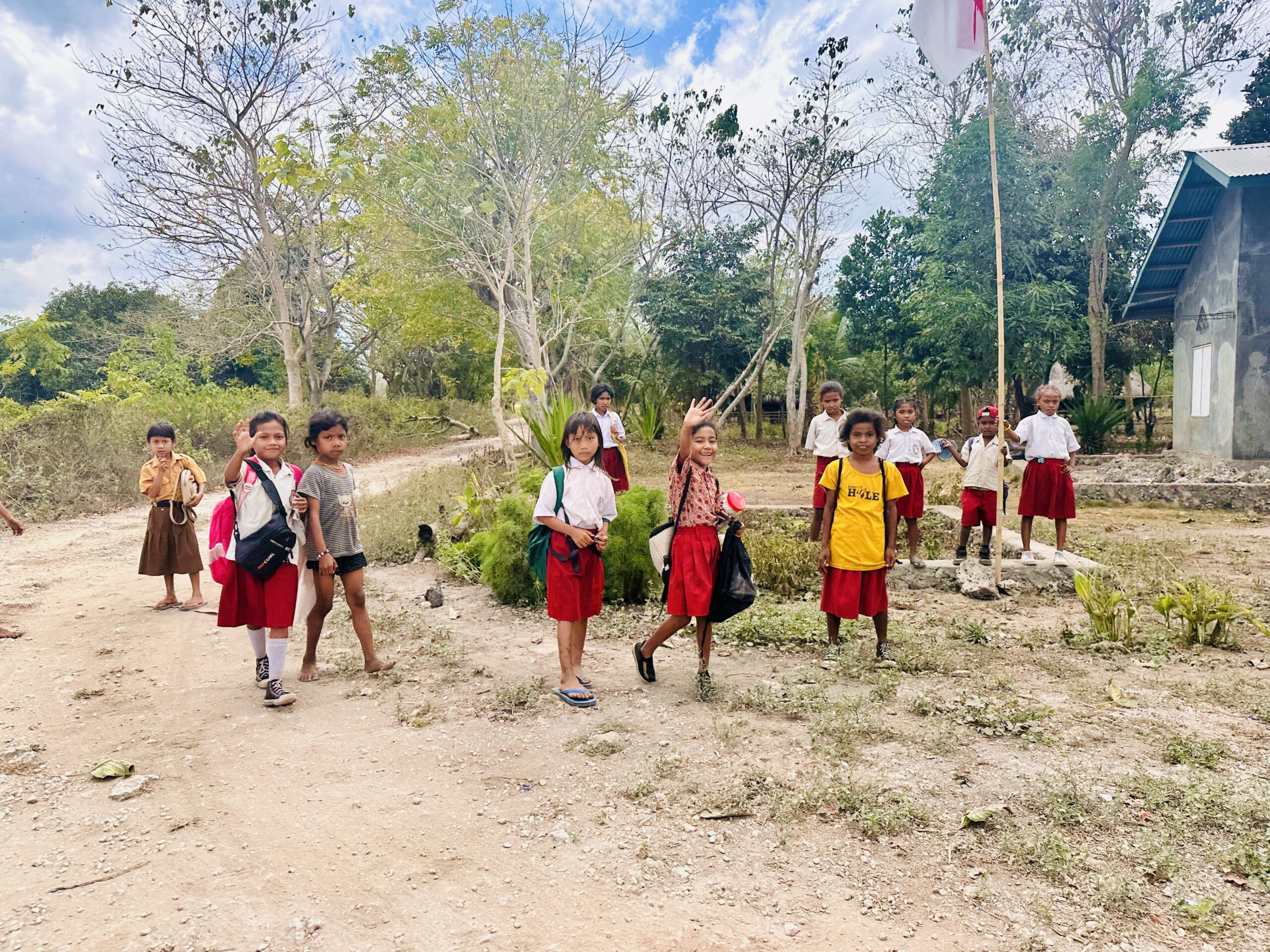 Groupe d'enfants de Sumba en uniforme scolaire souriants et saluant la caméra à l'extérieur d'une école